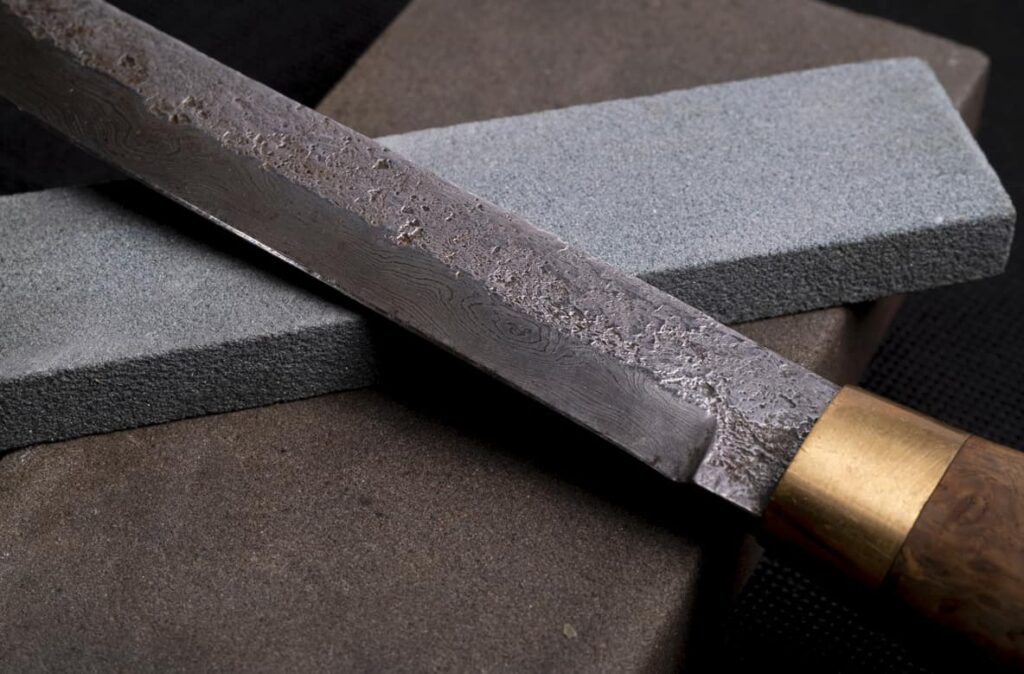 sharpening a Japanese knife with a whetstone. Beautiful wavy pattern of Damascus steel blade.