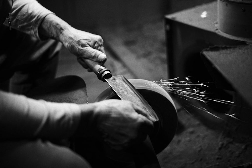 Hands sharpening a knife blade on a whetstone, showing the easy maintenance shared by both 12C27 and 14C28N steels